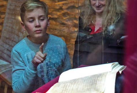 Ein Junge zeigt auf ein in einer Vitrine liegendes Buch